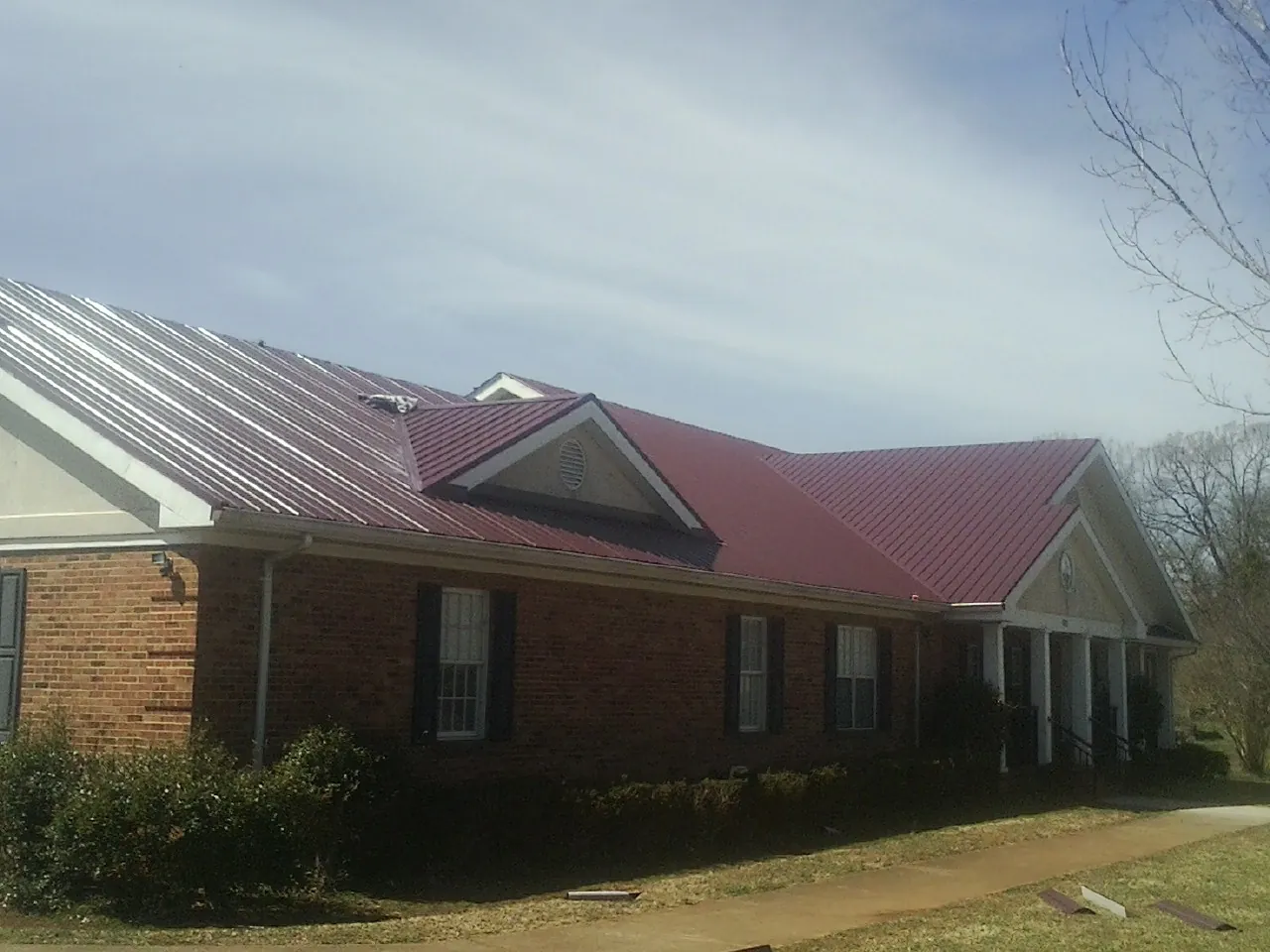 Red metal roof with gabled entries on a long brick building, from a Hail Damage Roof Repair job in Seven Valleys