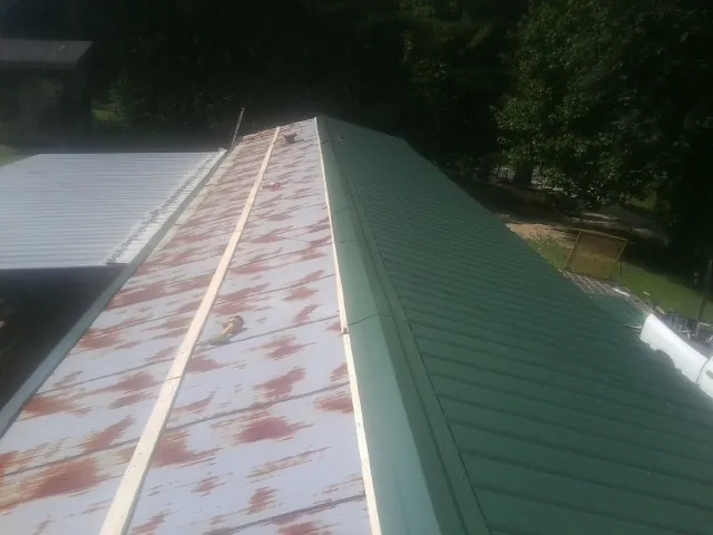 Old rusted panels beside newly installed green metal roofing — Wind Damage Roof Repair by Roofing Brothers in Seven Valleys