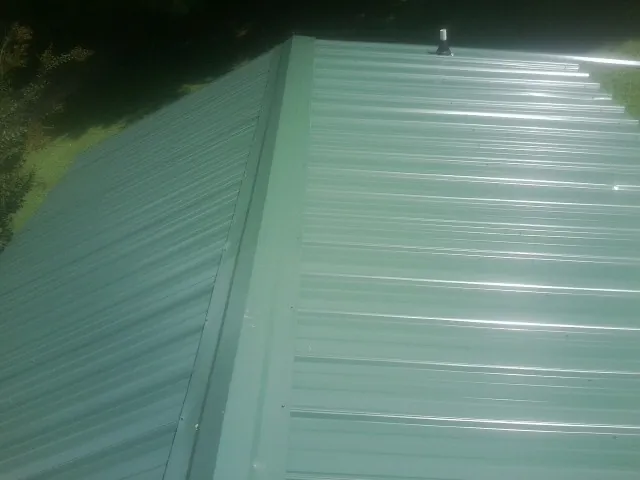 New green metal panels meeting at the ridge of a roof — Flat Roof Repair work by our crew in Seven Valleys