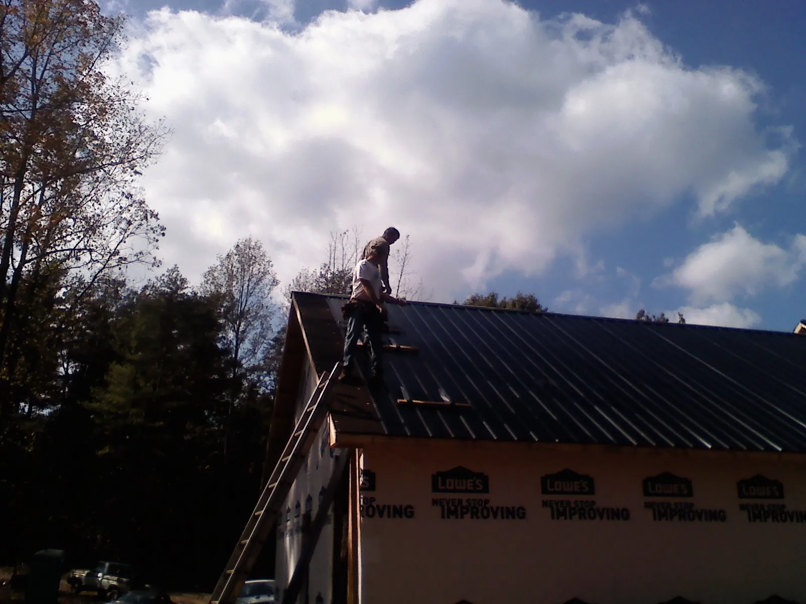 Roofer fastening dark metal panels high against a cloudy sky, from a Roof Inspection job in Seven Valleys