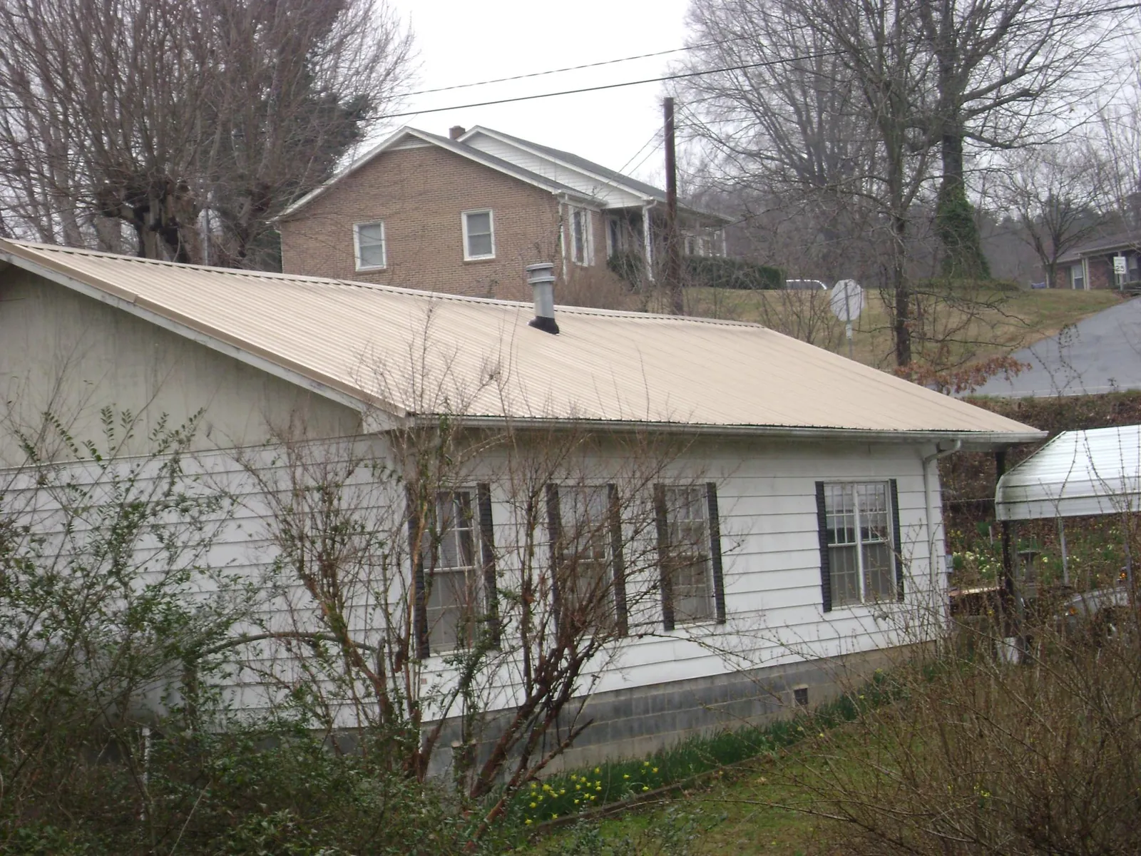 Tan metal roof on a white sided house set into a hillside — Commercial Roofing by Roofing Brothers in Seven Valleys